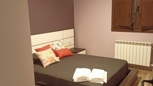 A neatly made bed with a dark bedspread, two pillows, and a folded towel. There is a wooden wardrobe with a radiator below it. - RURAL HOUSE THE VIEWPOINT OF SAN MIGUEL (San Esteban de Gormaz)