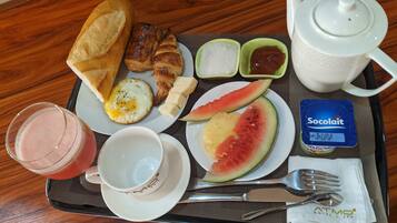 Un plateau de petit-déjeuner avec des croissants, des œufs, des toasts, de la pastèque, du yaourt et une boisson.
