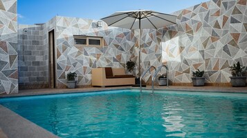 Zona de piscina con una pared de azulejos geométricos, una silla de descanso y plantas en macetas.