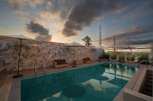 Una piscina con paredes de diseño geométrico, mobiliario exterior y sombrillas.