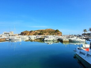 Boats docked in the marina reflect off the calm water, with a historic fort perched on the hill in the background.