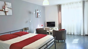 Una habitación de hotel moderna con una cama grande, un escritorio, una silla, un televisor de pantalla plana y un ventanal con cortinas.