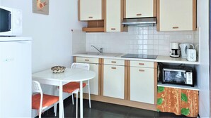 Una cocina compacta con microondas, tostadora y cafetera, una pequeña mesa de comedor con sillas y una lámpara empotrada en la pared.