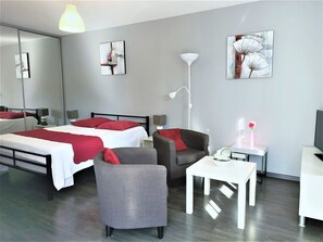 A modern hotel room with a bed, two chairs, a small table, a desk, a lamp, and artwork on the walls.