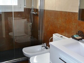 Casa de banho com cabine de chuveiro em vidro, sanita, bidé e lavatório com espelho.