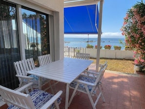 Um pátio com mesa e cadeiras, um toldo azul e vista para o mar.