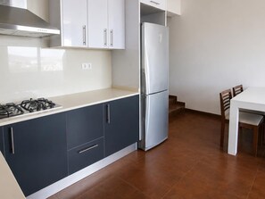 A kitchen with dark cabinets, a white countertop, a stainless steel refrigerator, and a dining table with chairs.