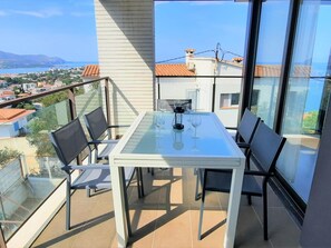 Enjoy a relaxing moment on this balcony with a glass-top table and four comfortable chairs, offering a serene view of the surrounding houses and the distant sea.