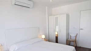 A hotel room with a bed, a wardrobe, a chair, and an air conditioning unit.