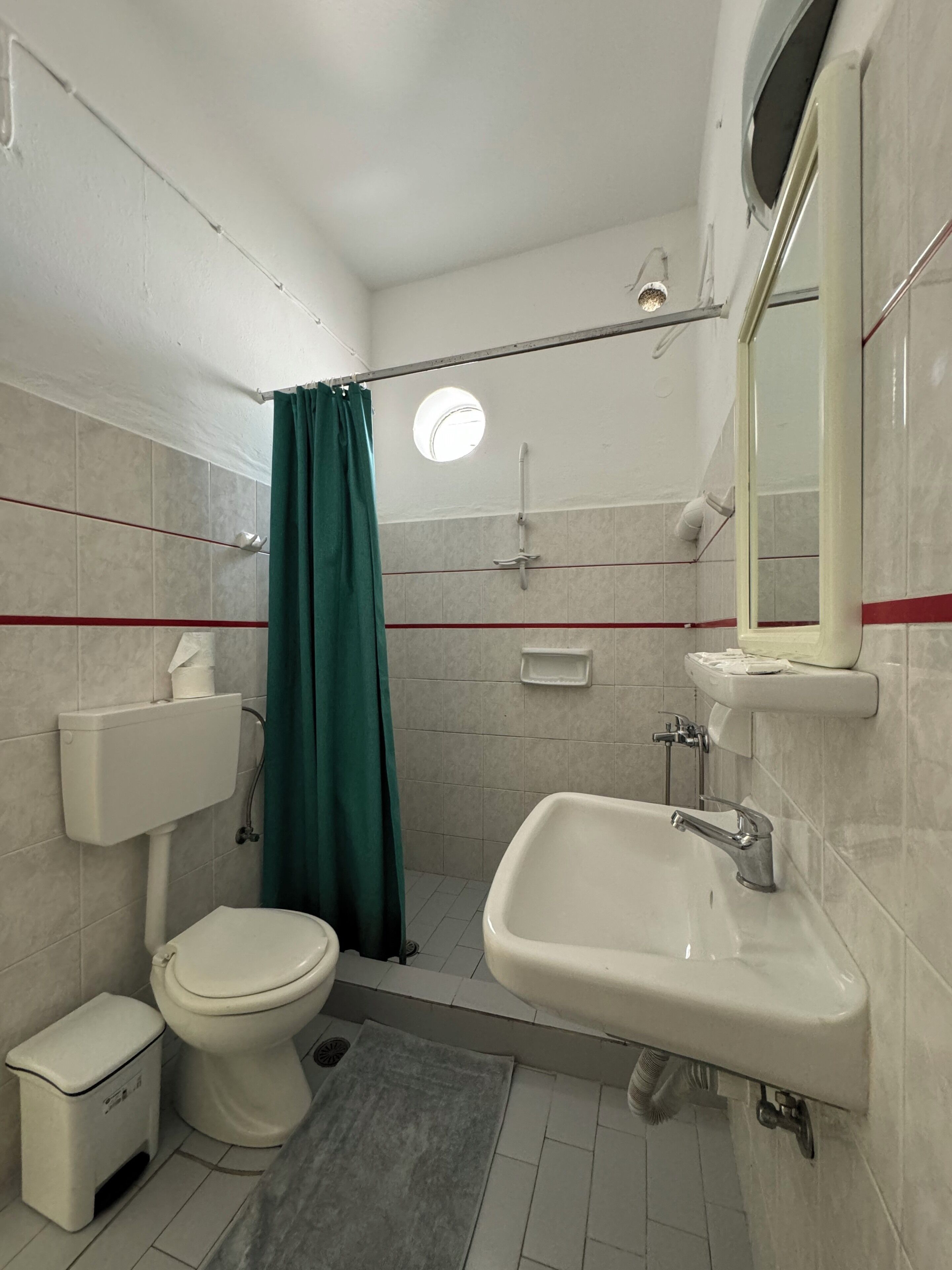 A compact bathroom with a toilet, sink, shower, and a small mirror.