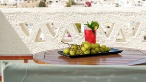 Una mesa con un plato de uvas verdes y una bebida roja, frente a una vista de edificios blancos en una colina.
