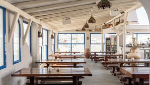 Un café espacioso con mesas y bancos de madera, ventanas amplias y faroles colgantes.