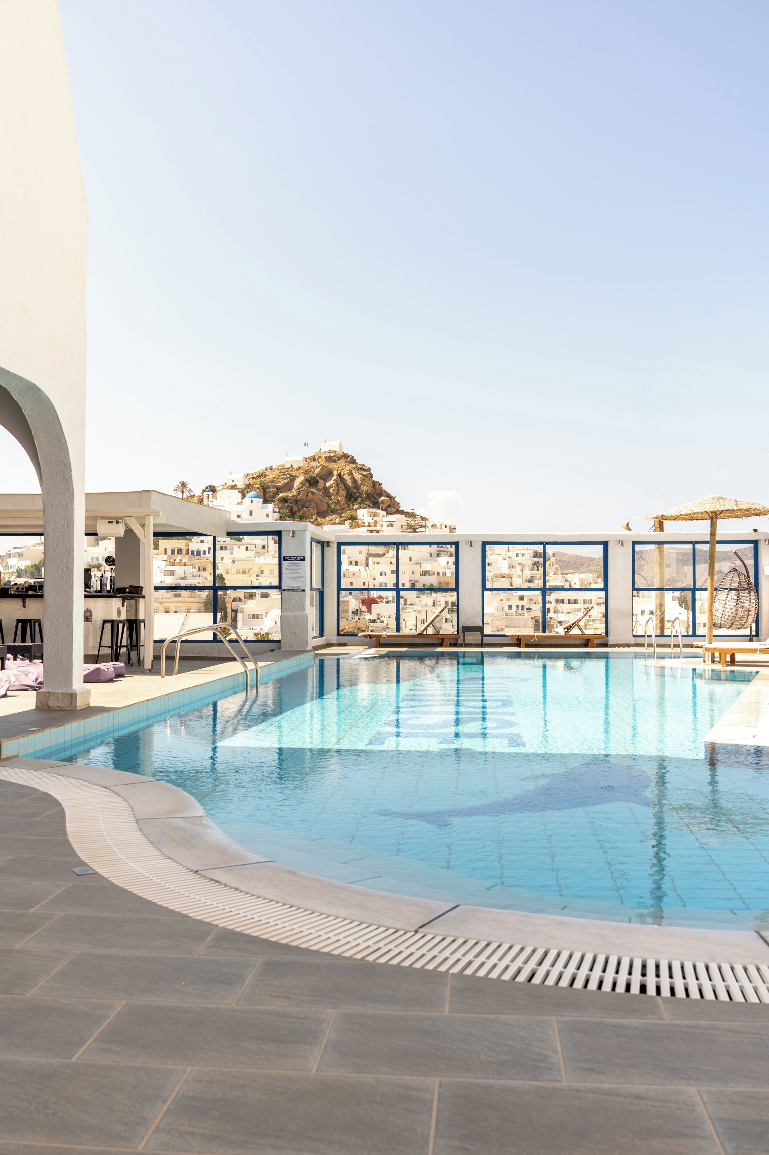 A rooftop pool with clear views of a mountainous landscape, a bar area, and a seating area with umbrellas.