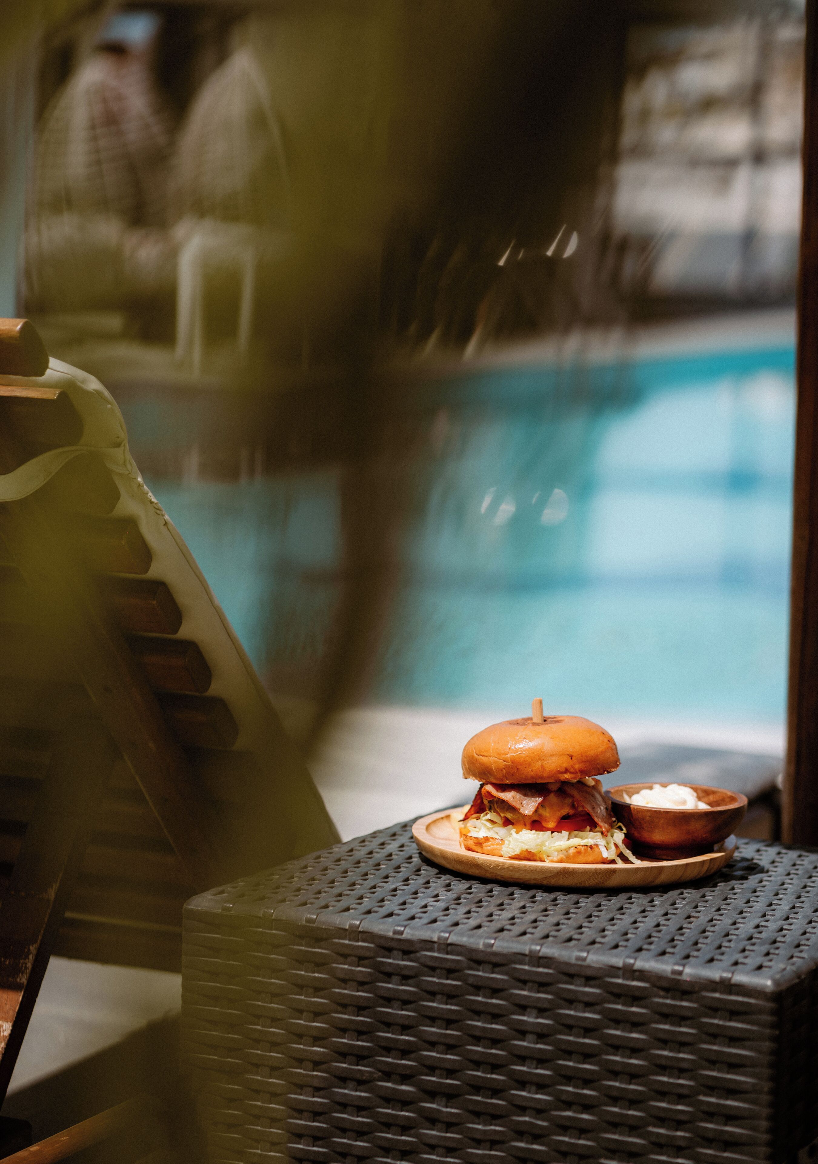 Un coin repas avec vue sur la piscine, un sandwich sur une assiette et un petit bol de sauce.