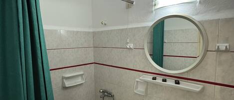Un baño con ducha, lavamanos, espejo y toallero.