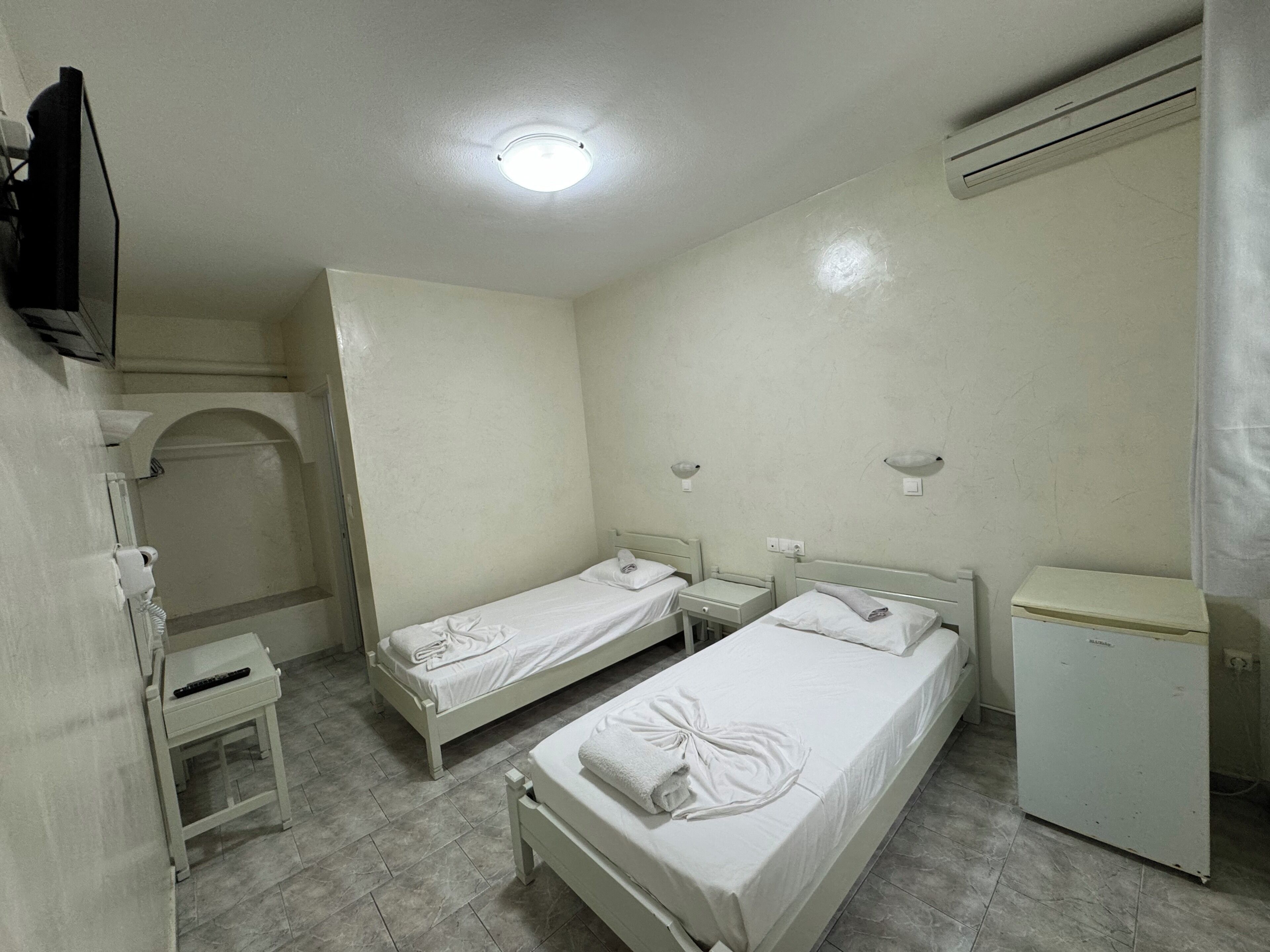 A room with two single beds, a small desk, a TV, and a mini-fridge.