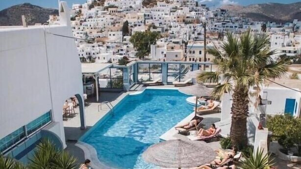 Zona de piscina en la azotea con sillones de descanso y sombrillas, con vistas a un pueblo encalado y una colina destacada.