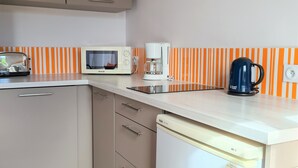 La cuisine est équipée d’un four à micro-ondes, d’une machine à café et d’un lave-vaisselle. Il y a une horloge au mur et une étagère où sont rangés les ustensiles de cuisine.