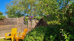 Un jardin avec une clôture en bois, deux chaises jaunes et diverses plantes et fleurs.