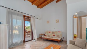 A cozy living room with a sofa, a wooden table, and a balcony with a view. - APARTMENT WITH SEA VIEW VERANDA 5 MINUTES FROM THE BEACH (Golfo Aranci)