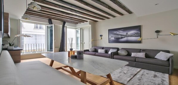 A modern living room with a sofa, a dining table, and a view of the city through large windows.