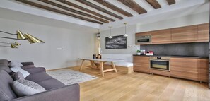 A modern living room with a sofa, a dining table, and a kitchen area with wooden cabinets and appliances.