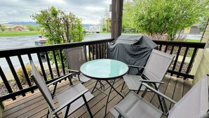 Een overdekt terras met een glazen tafel en vier stoelen, met uitzicht op water en groen.