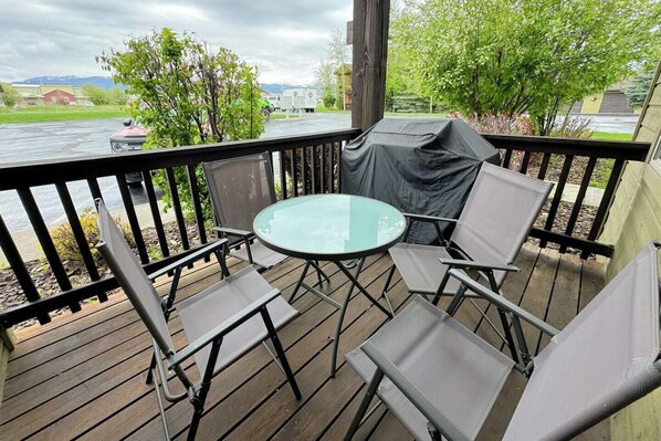 Une terrasse extérieure couverte, dotée d’une table en verre et de quatre chaises, qui offre une vue sur une étendue d’eau et la verdure environnante.