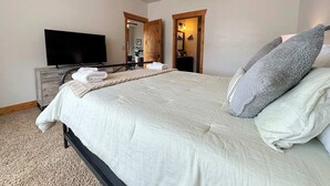 Een slaapkamer met een bed, een televisie, een plafondventilator en een houten deur.