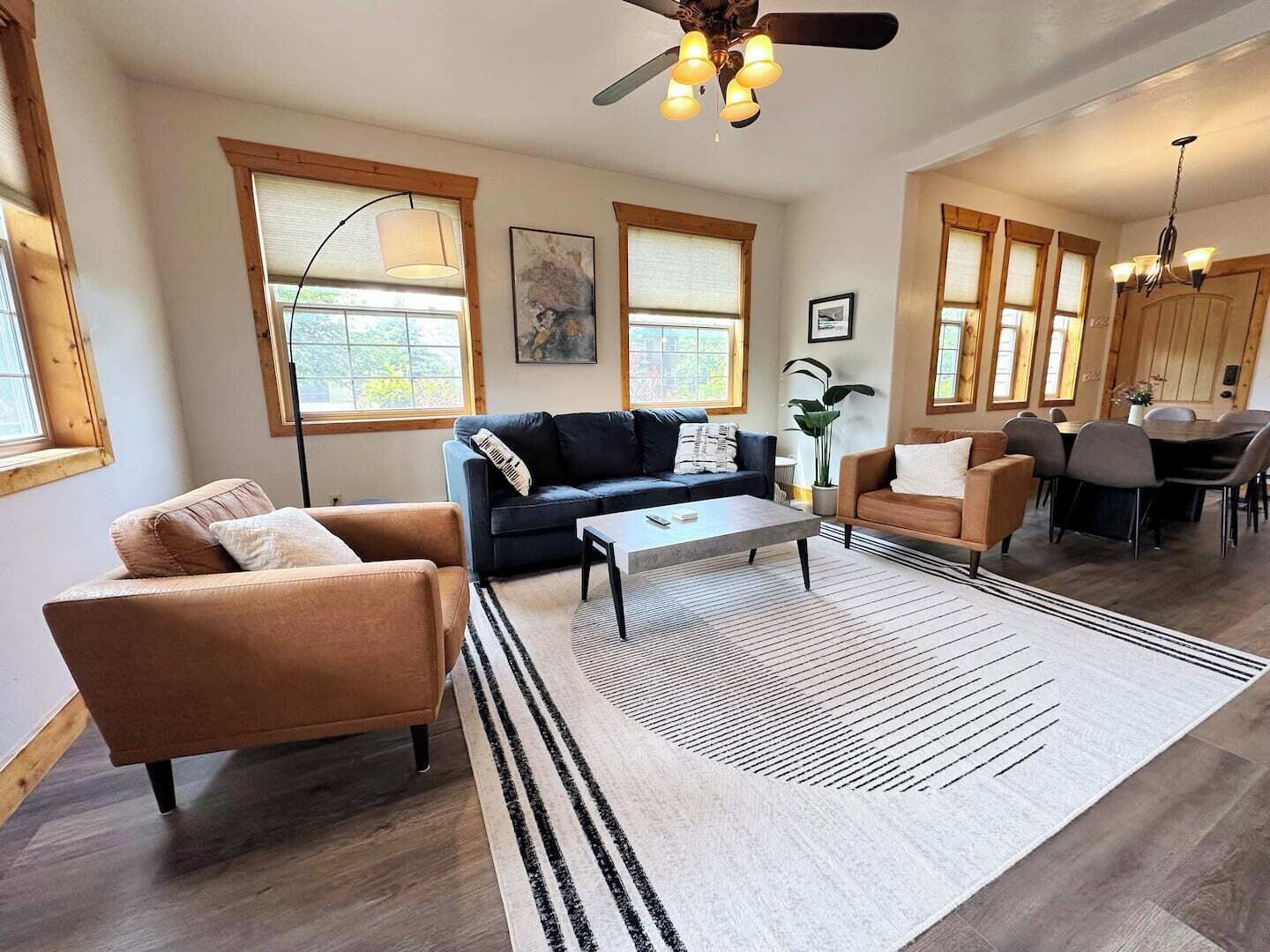 Un salón amplio con sofá, sillón y mesa de centro, un comedor con sillas y una mesa, y ventanas grandes con persianas.