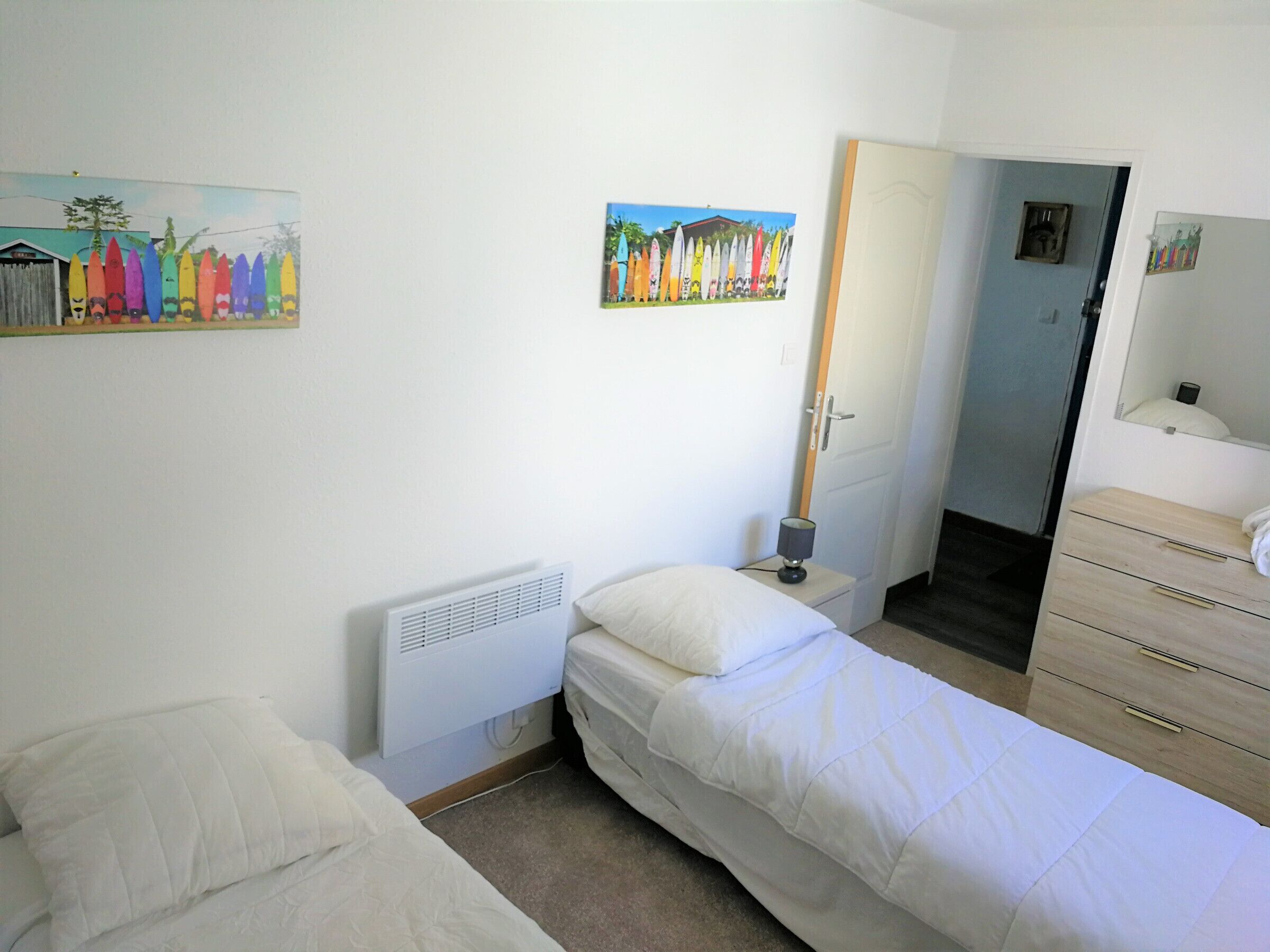 A bedroom with a bed, a bedside table with a lamp, a dresser, and two wall-mounted paintings.