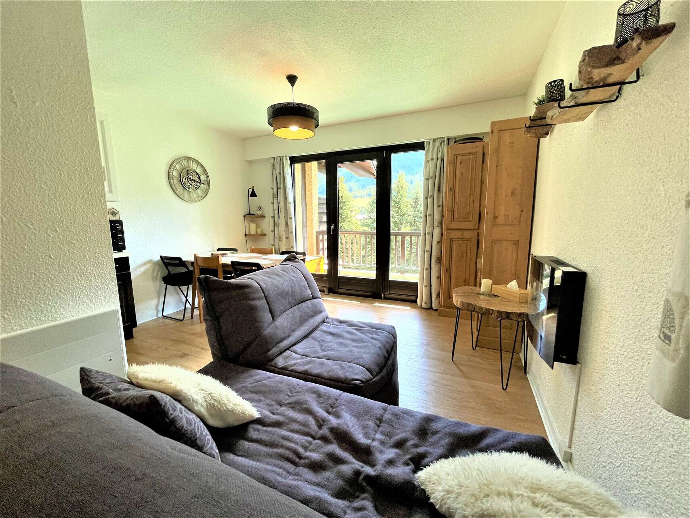 Ett mysigt vardagsrum med en soffa, en matplats med bord och stolar, ett stort fönster med gardiner och en taklampa.