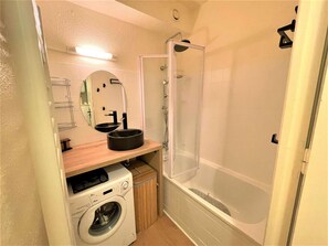 A compact bathroom with a washing machine, a sink with a mirror, and a shower enclosure.