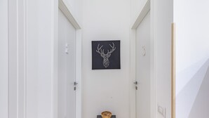 Un pasillo con un cuadro de un venado en la pared, una pequeña mesa de madera con un cuenco, y una puerta a la derecha.