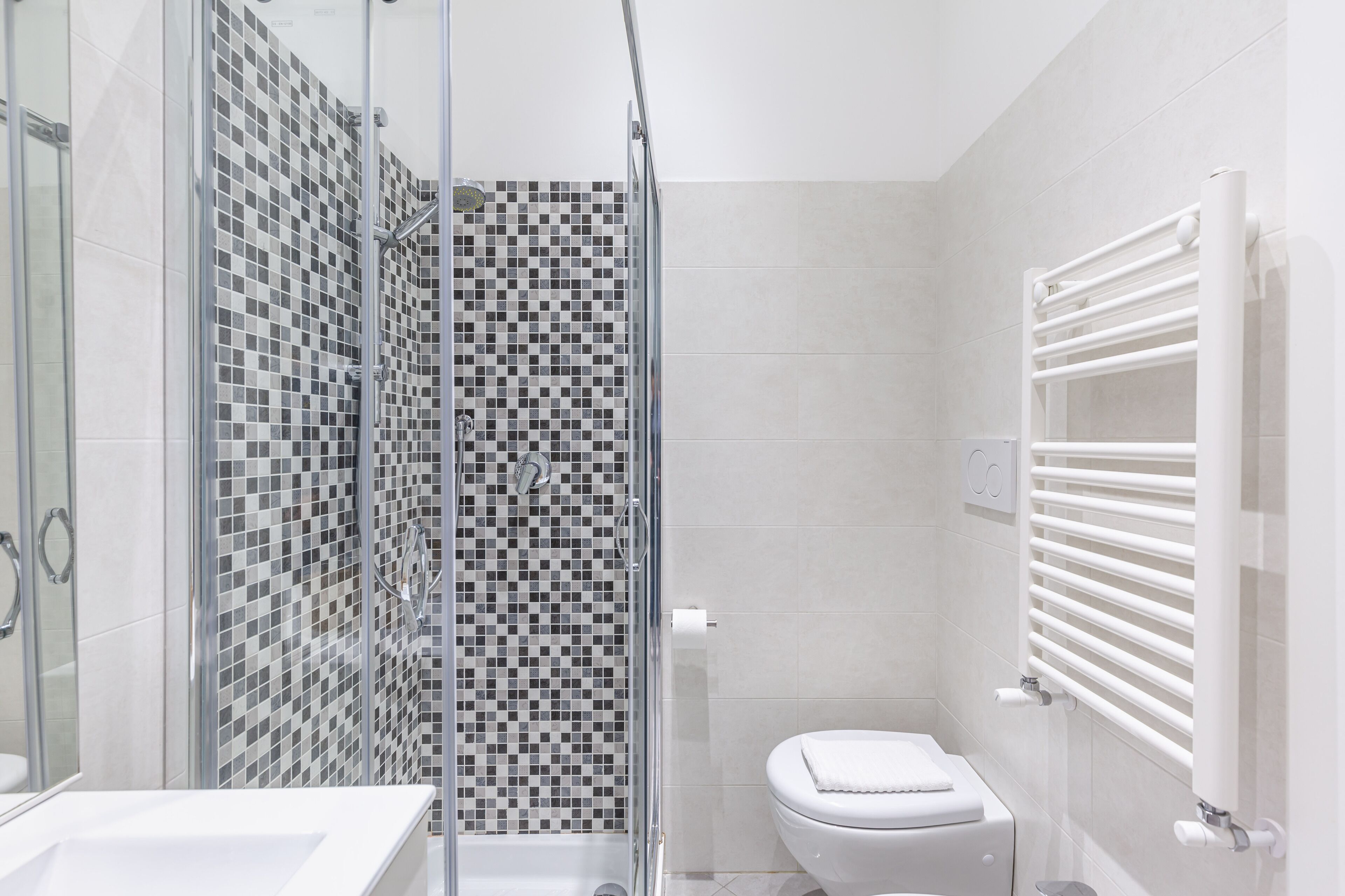 A modern bathroom with a glass shower enclosure, a white toilet, and a white towel rack.