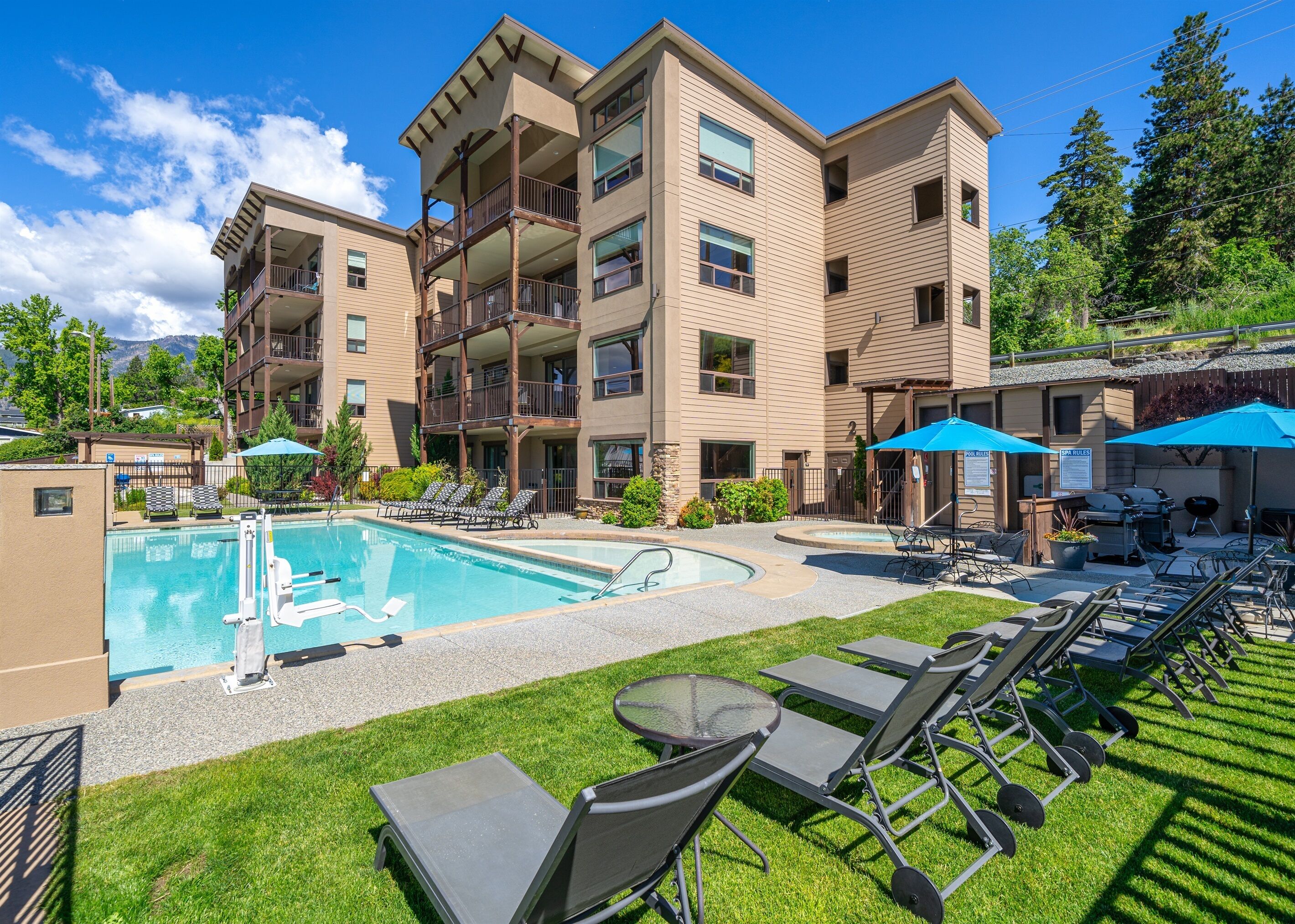 A multi-story hotel with a swimming pool, outdoor seating, and a well-maintained lawn.