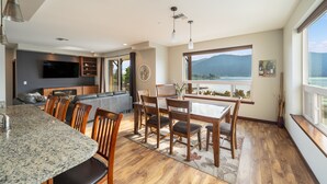 A modern kitchen with a dining area, large windows with a mountain view, and a flat-screen TV mounted on the wall. - Breathtaking views, walk downtown-Manson Bay (Manson)