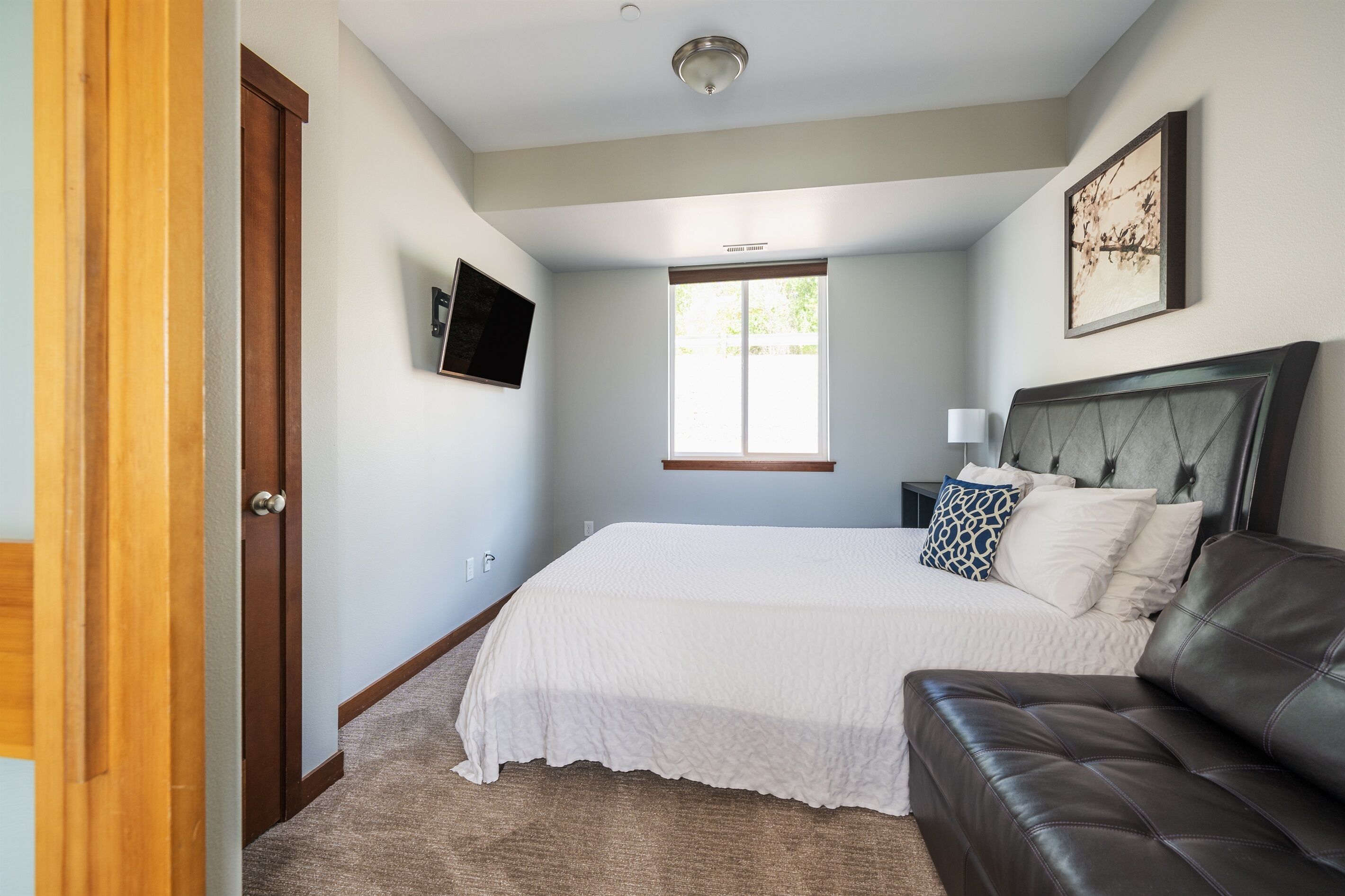 A bedroom with a bed, a nightstand, a TV mounted on the wall, a window, and a door.
