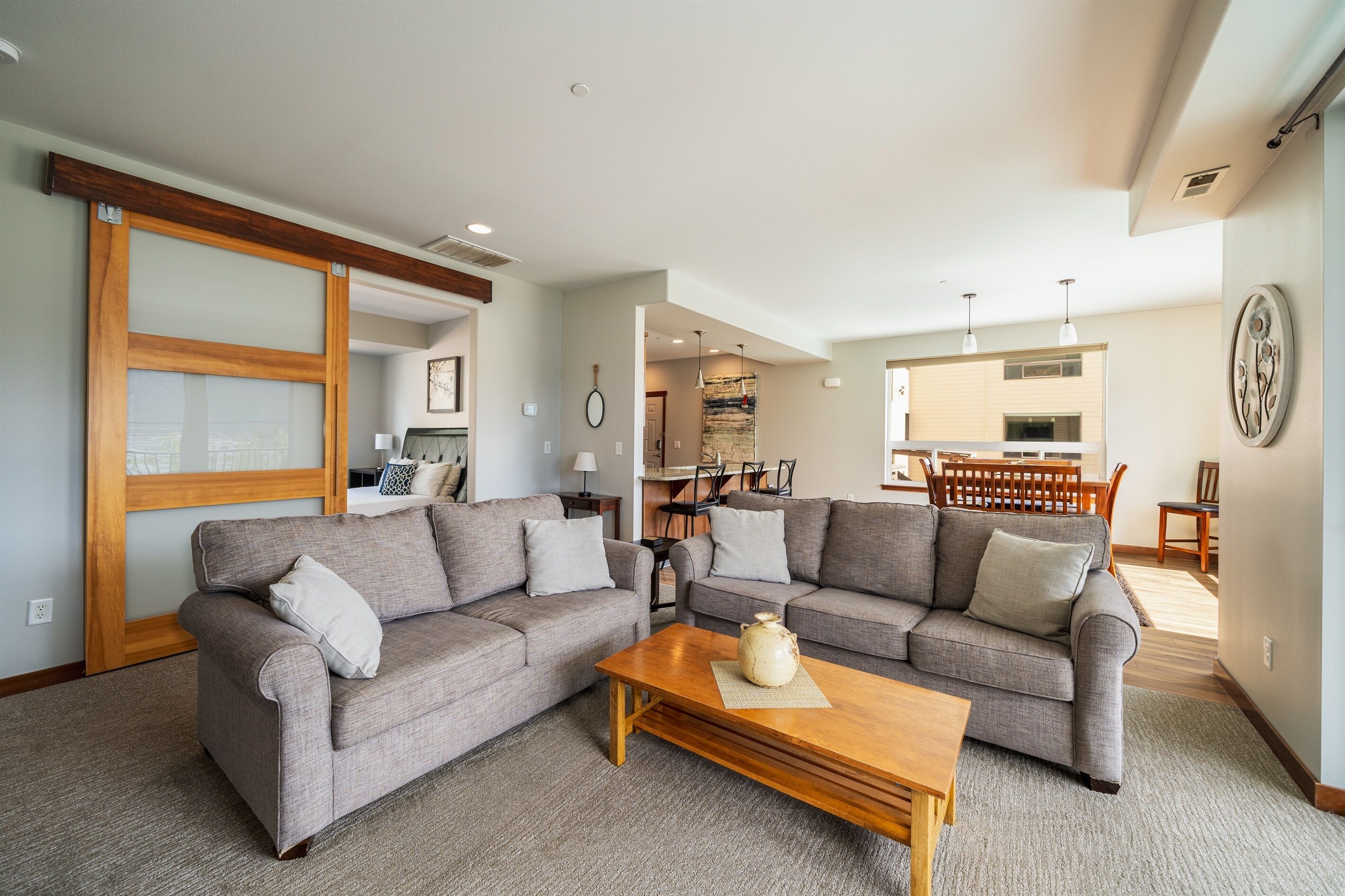 A living room with two grey sofas, a wooden coffee table, and a kitchen area in the background.