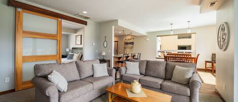 A living room with two grey sofas, a wooden coffee table, and a kitchen area in the background.