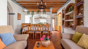 A cozy living room with a wooden ceiling, a dining area with a table and chairs, and a kitchen with shelves and a brick oven. - Casa Mora + Caminito del Rey (Ardales, Malaga) (Ardales)
