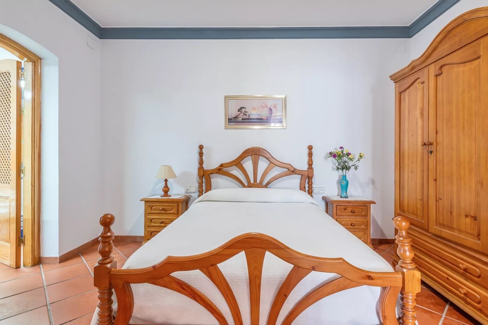 Une chambre à coucher avec un lit en bois, une table de chevet avec une lampe, une commode et un tableau encadré au mur.