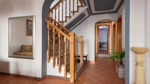 A spacious hallway with a wooden staircase, a seating area with a sofa, and a potted plant. - Casa Mora + Caminito del Rey (Ardales, Malaga) (Ardales)