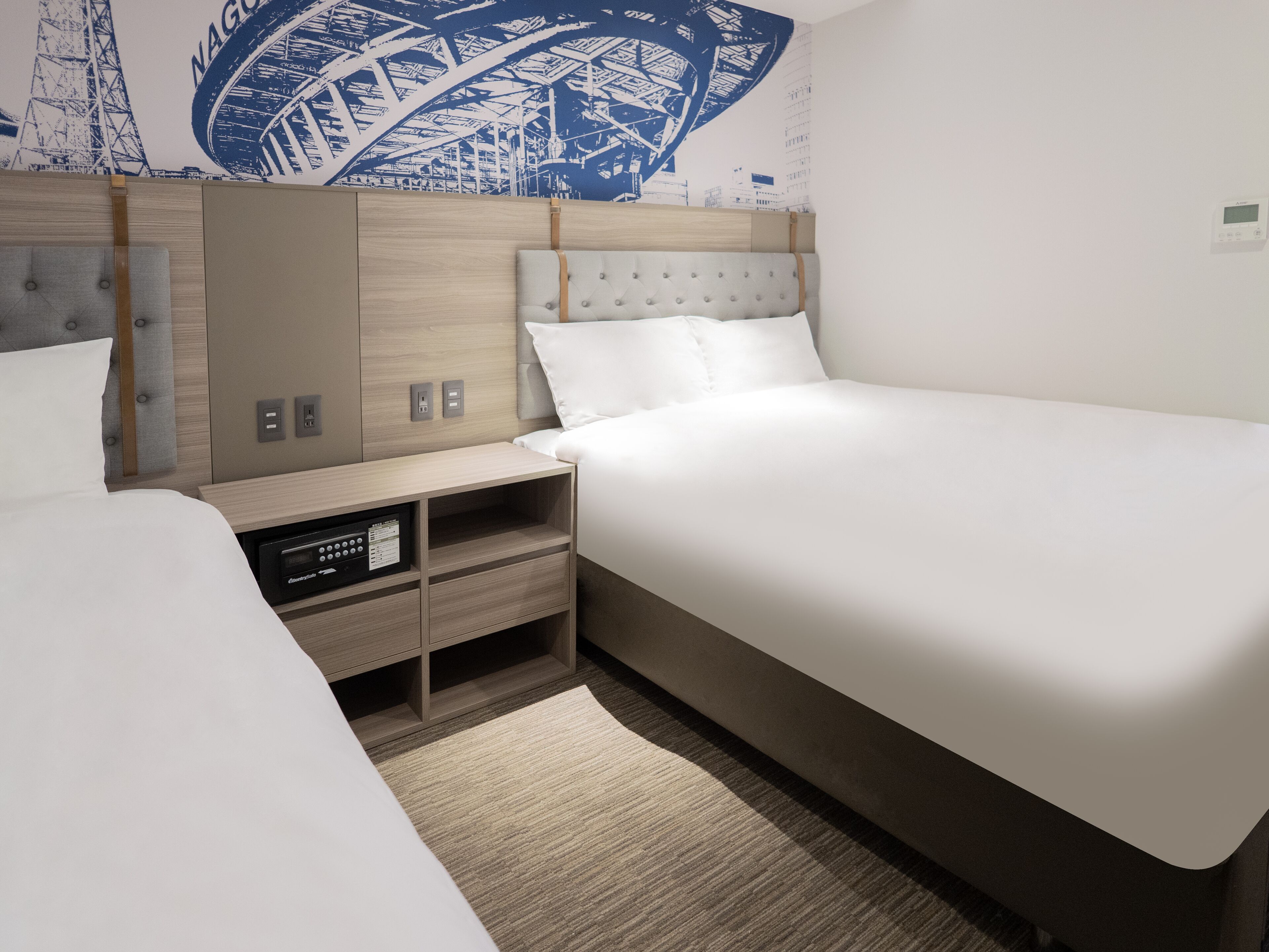A modern hotel room with a large bed, a bedside table with a radio, a nightstand, and a wall mural.