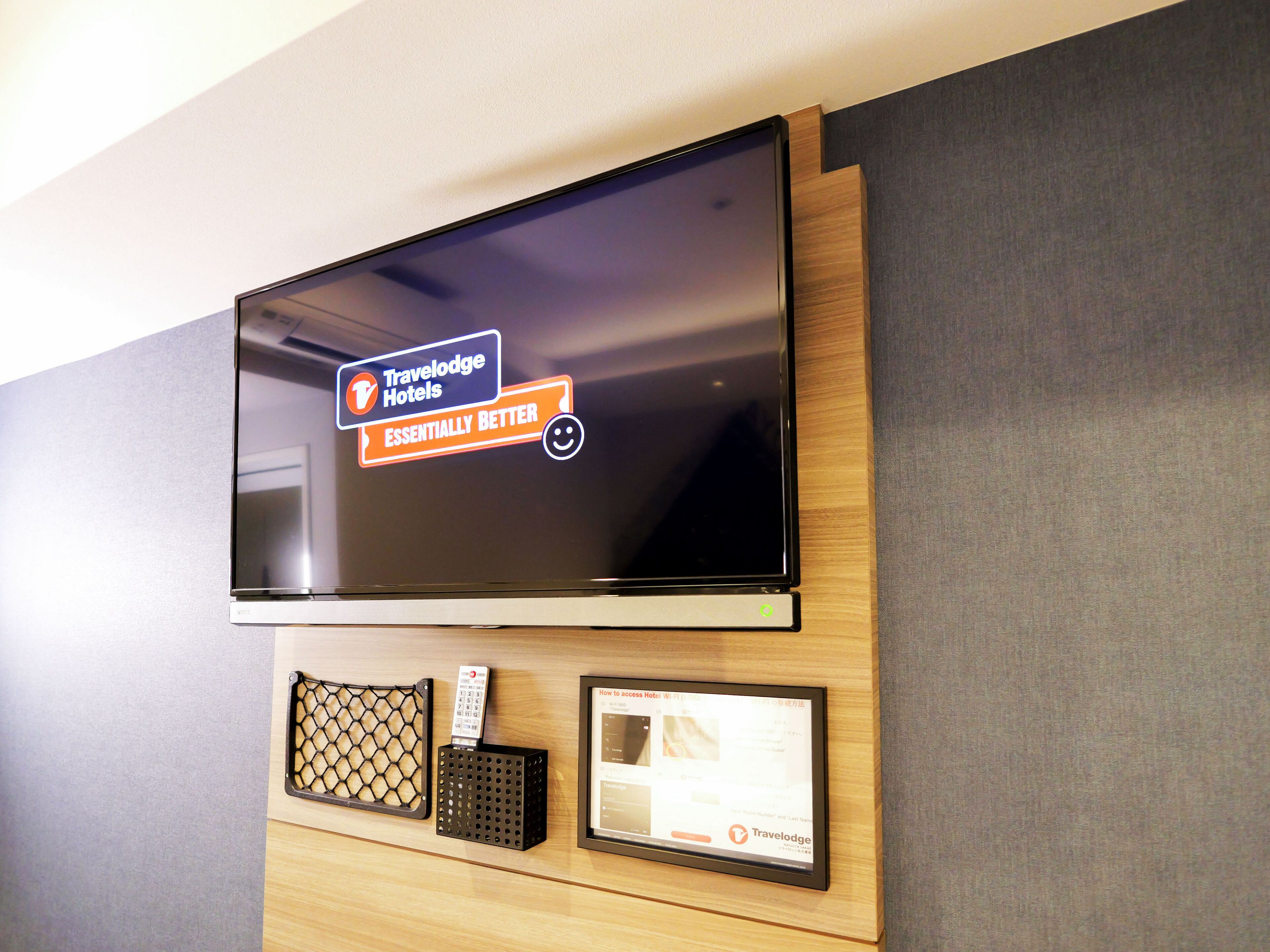 A flat-screen TV mounted on a wooden wall with a Travelodge Hotels logo and a Wi-Fi access guide.
