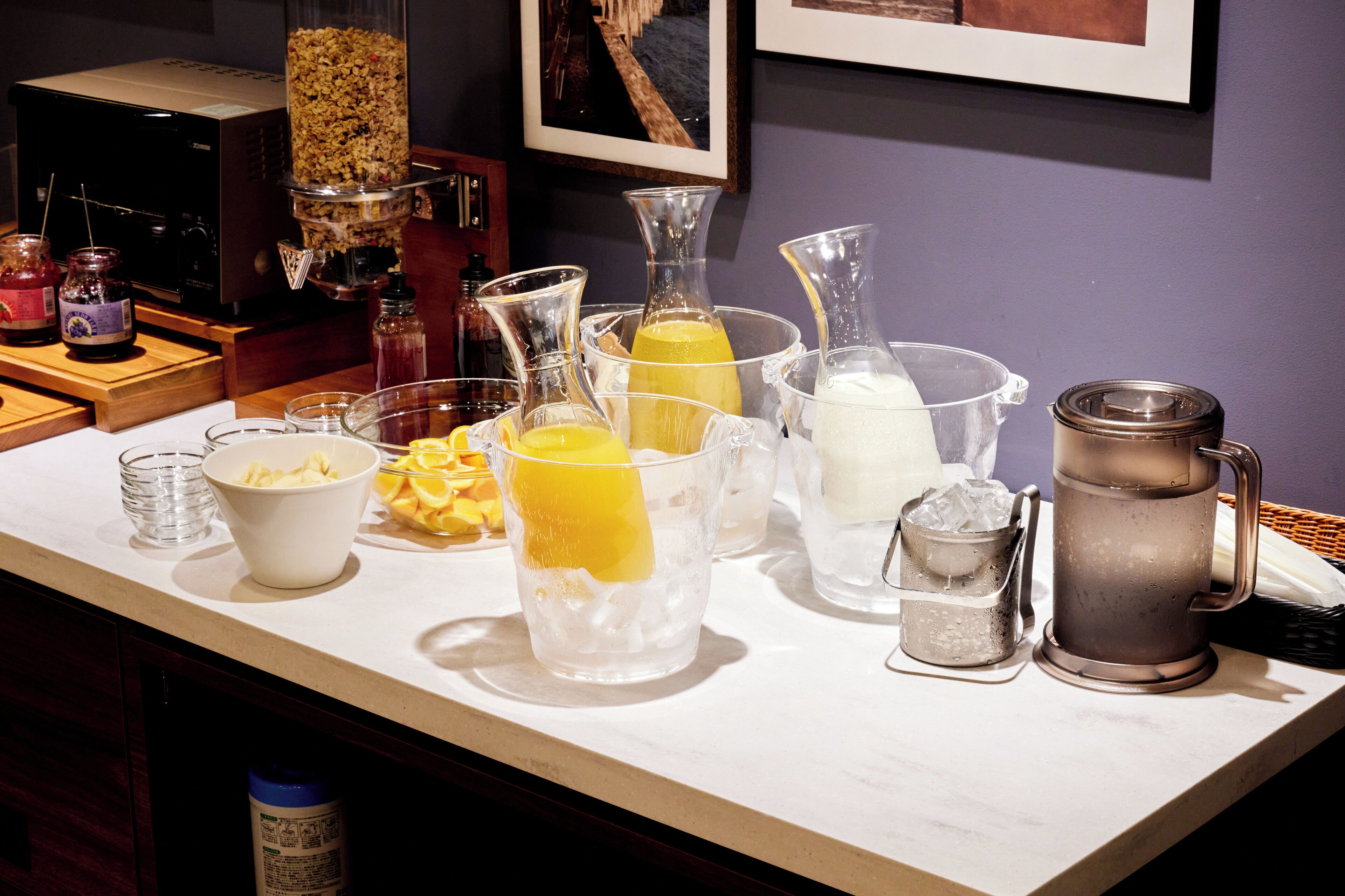 Una zona de bar con diversos utensilios e ingredientes para preparar bebidas, incluyendo vasos, un exprimidor y una cafetera.