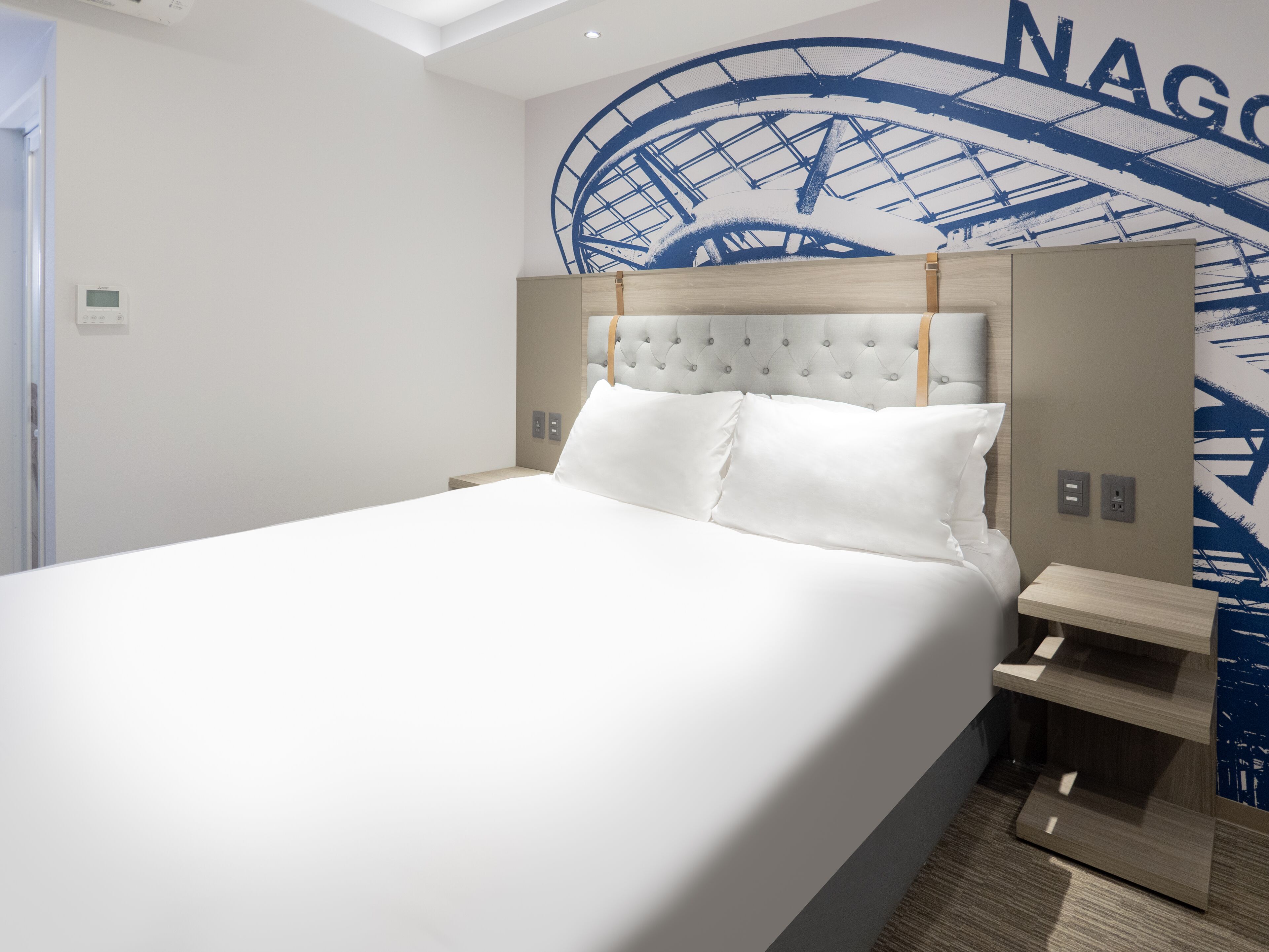 A modern hotel room with a large bed, a headboard with a tufted design, bedside tables, and a wall mural.