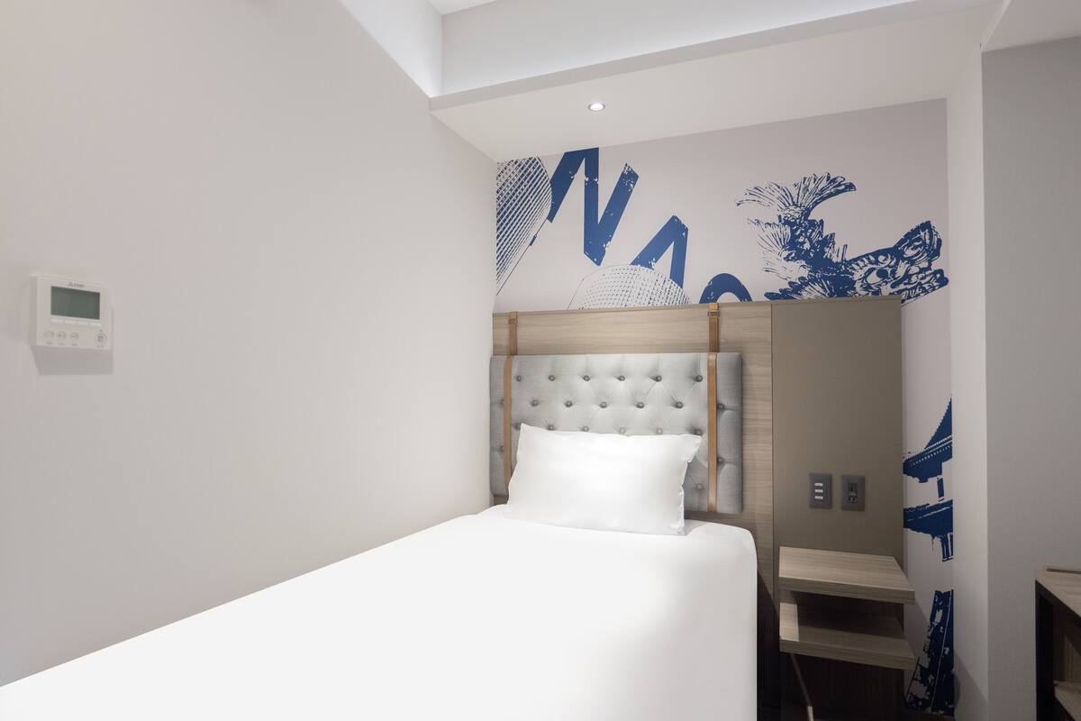 Une chambre d’hôtel moderne avec un lit soigneusement fait, une tête de lit au motif capitonné et un panneau de commande fixé au mur.