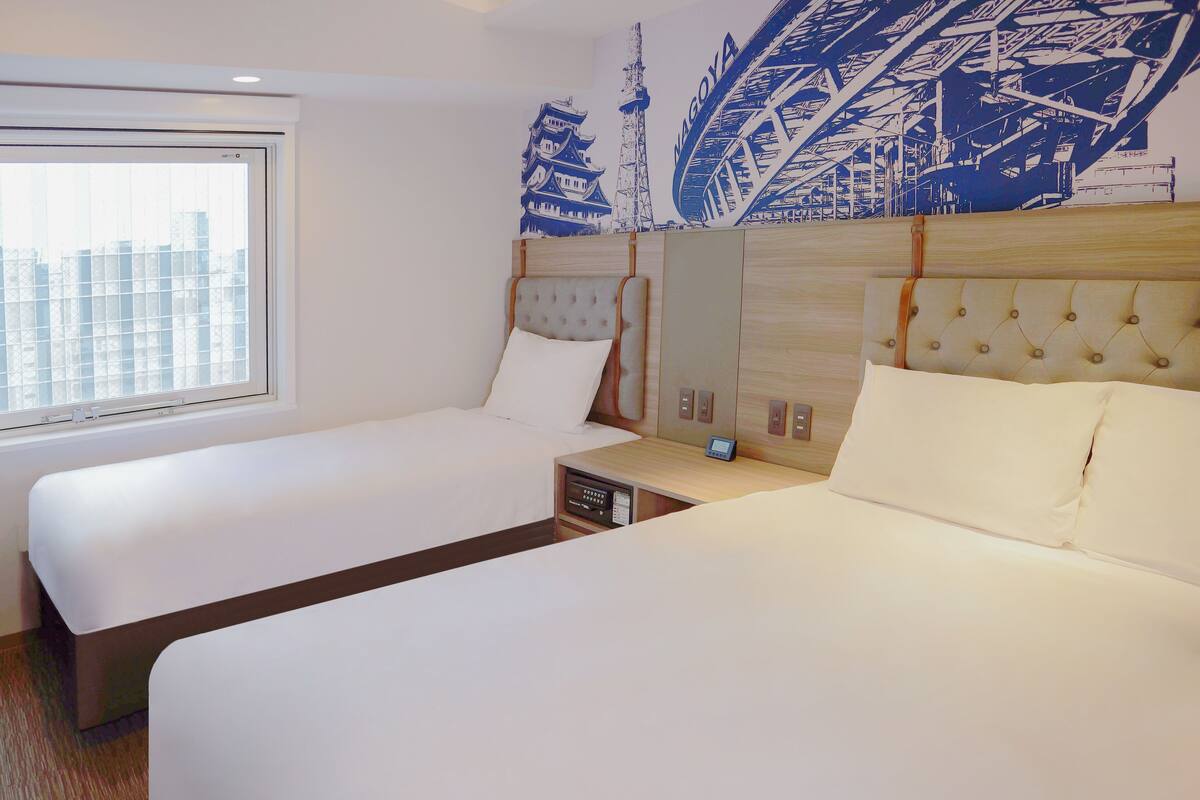 Une chambre d’hôtel avec deux lits, une grande fenêtre et une fresque représentant un bâtiment traditionnel.