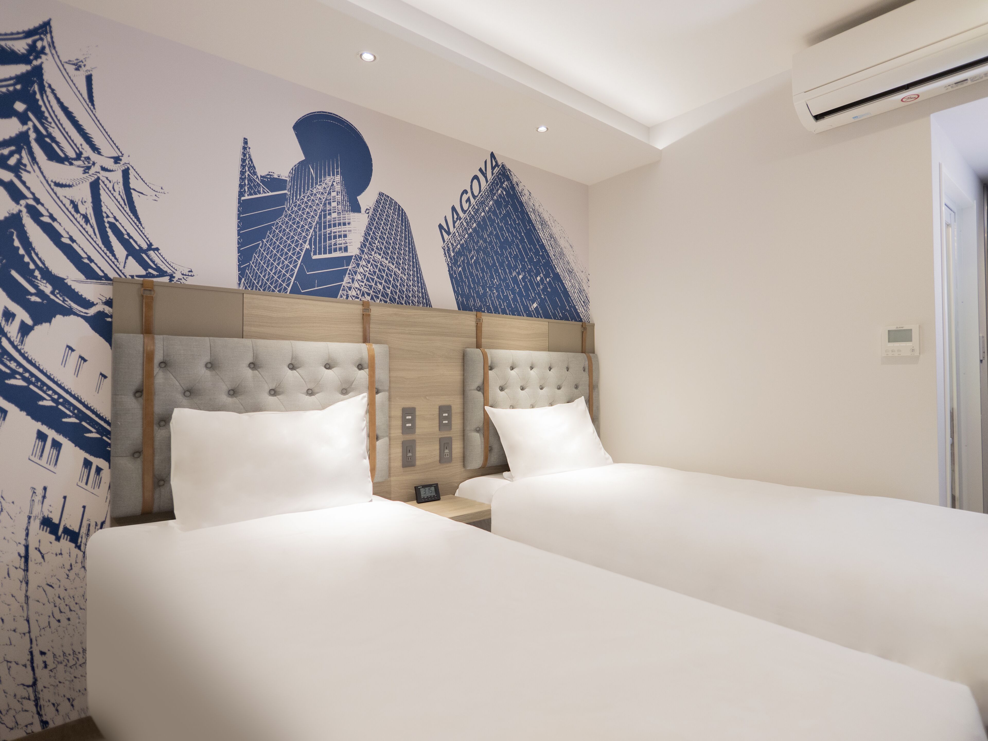 A hotel room with a large bed, a headboard with a wooden panel, and a wall mural of city buildings.